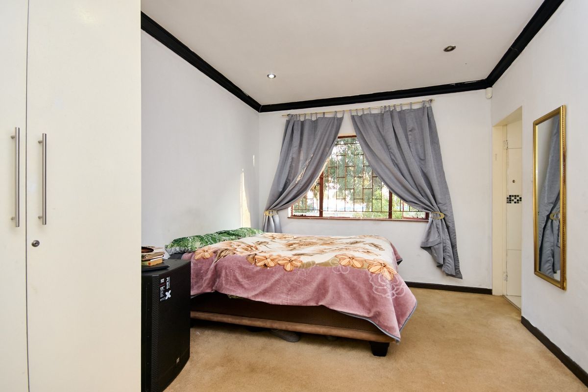 A bedroom featuring built-in wardrobes, recessed downlighting, and security bars on the window. The room includes carpet flooring and decorative cornice detailing.
