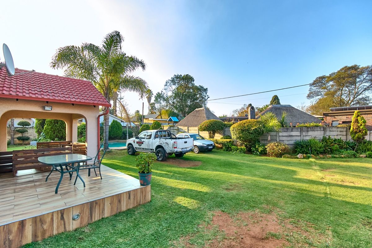 Spacious rear garden featuring a covered tiled patio, swimming pool, and well-maintained lawn area, providing an ideal space for outdoor relaxation and entertainment.