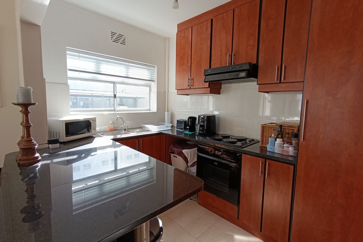 A functional kitchen featuring dark granite countertops, wooden cabinetry, built-in oven and hob, and a tiled backsplash with a window for natural light.