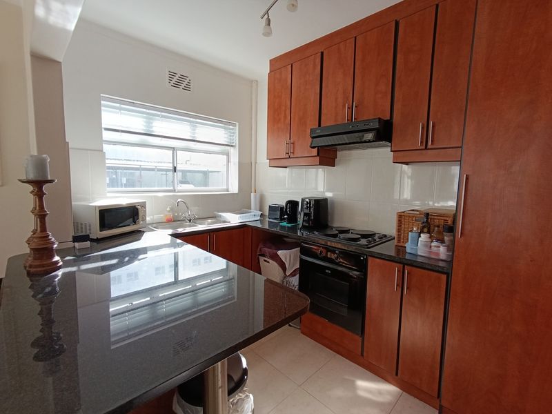 A functional kitchen featuring dark granite countertops, wooden cabinetry, built-in oven and hob, and a tiled backsplash with a window for natural light.