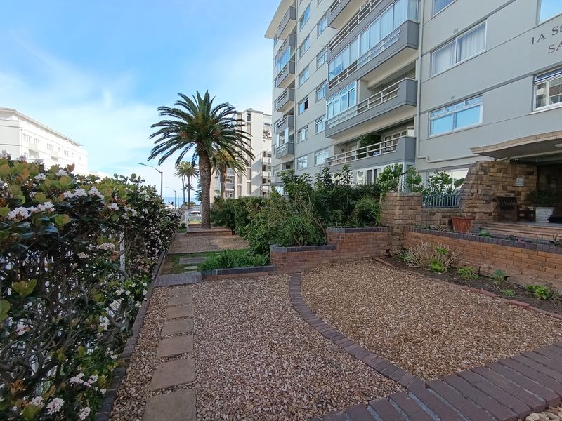 Front exterior view of the apartment building featuring landscaped gravel gardens, stone-clad entrance details, and multi-story residential balconies.