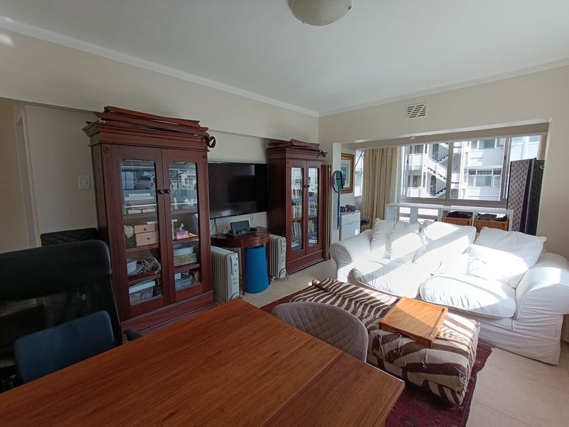 A spacious living room featuring tiled flooring, large windows allowing natural light, and a neutral wall finish, providing a comfortable and functional living space.