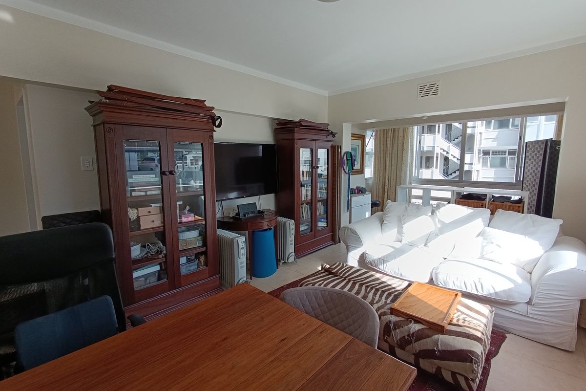 A spacious living room featuring tiled flooring, large windows allowing natural light, and a neutral wall finish, providing a comfortable and functional living space.