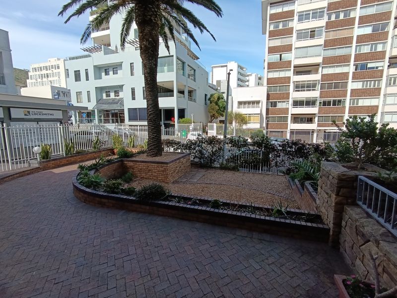 A paved front courtyard area featuring brick planter boxes, a mature palm tree, and metal security fencing in an urban apartment setting.
