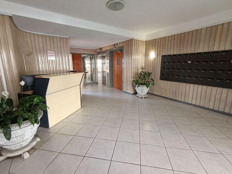 Apartment building entrance lobby featuring a reception desk, elevator access, and a wall-mounted bank of mailboxes with tiled flooring.