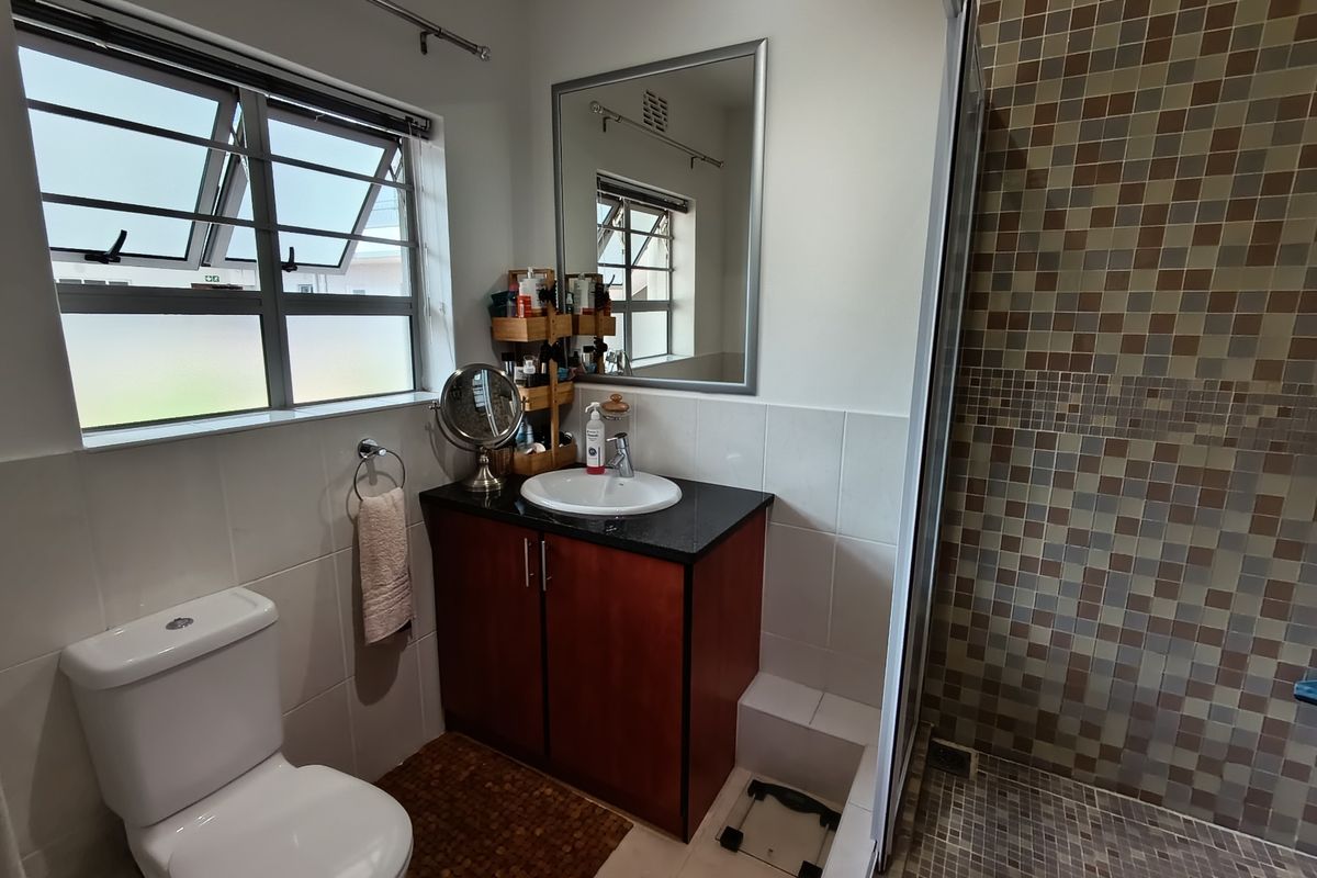 A functional bathroom featuring a vanity with granite countertop, a toilet, and a shower enclosure with mosaic tile accents.