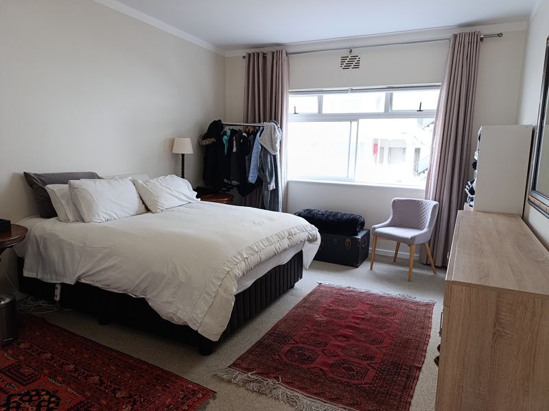 A well-lit bedroom featuring neutral walls, carpeted flooring, and a large sliding window with curtain fixtures.