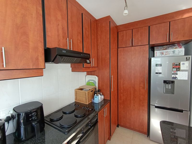 A functional kitchen featuring wood-finish cabinetry, granite countertops, a built-in electric hob, oven, and extractor fan with a tiled backsplash.