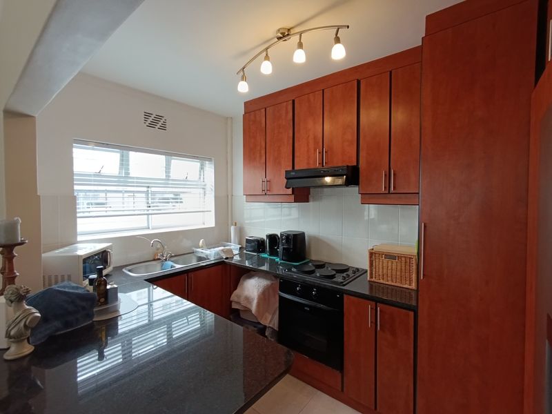 A functional kitchen featuring warm-toned wooden cabinetry, dark granite countertops, a built-in oven with hob, and a tiled backsplash.