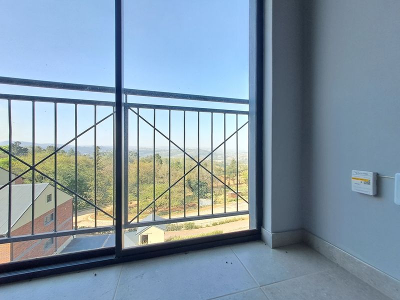 A clean, modern balcony featuring a metal balustrade and sliding glass doors, offering an elevated view of the surrounding landscape.
