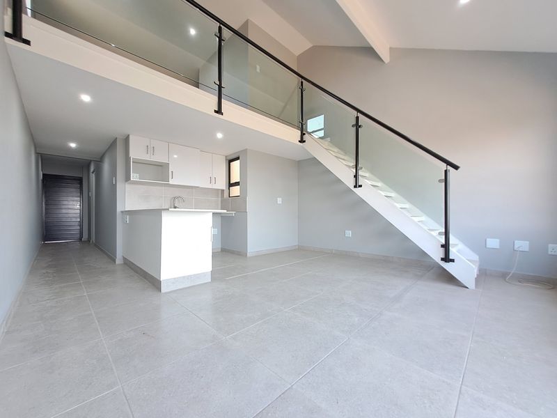 Modern open-plan living area featuring a sleek kitchen, tiled floors, and a contemporary staircase with a glass balustrade leading to a mezzanine level.