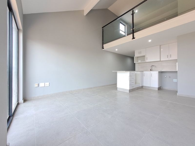 Modern open-plan living area featuring large format floor tiles, a sleek kitchen with white cabinetry, and a mezzanine level with a contemporary glass balustrade.