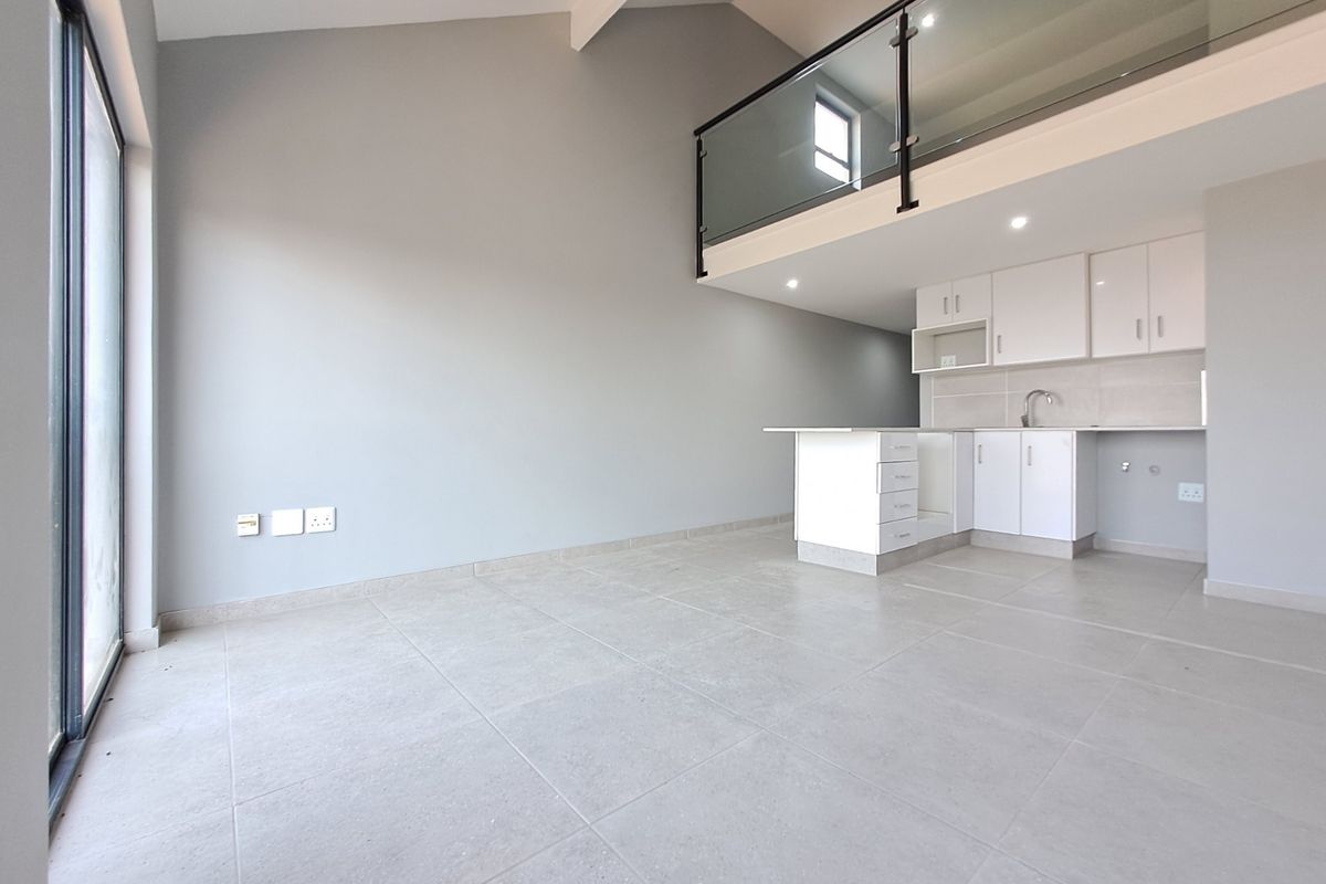 Modern open-plan living area featuring large format floor tiles, a sleek kitchen with white cabinetry, and a mezzanine level with a contemporary glass balustrade.