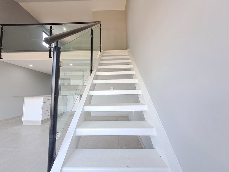 Modern staircase featuring a sleek glass balustrade and white treads, connecting levels in this contemporary apartment interior.