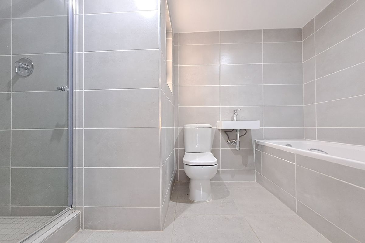 A modern, neutral-toned bathroom featuring a glass-enclosed shower, a built-in bathtub, a wall-mounted basin, and a toilet, finished with contemporary ceramic tiling.