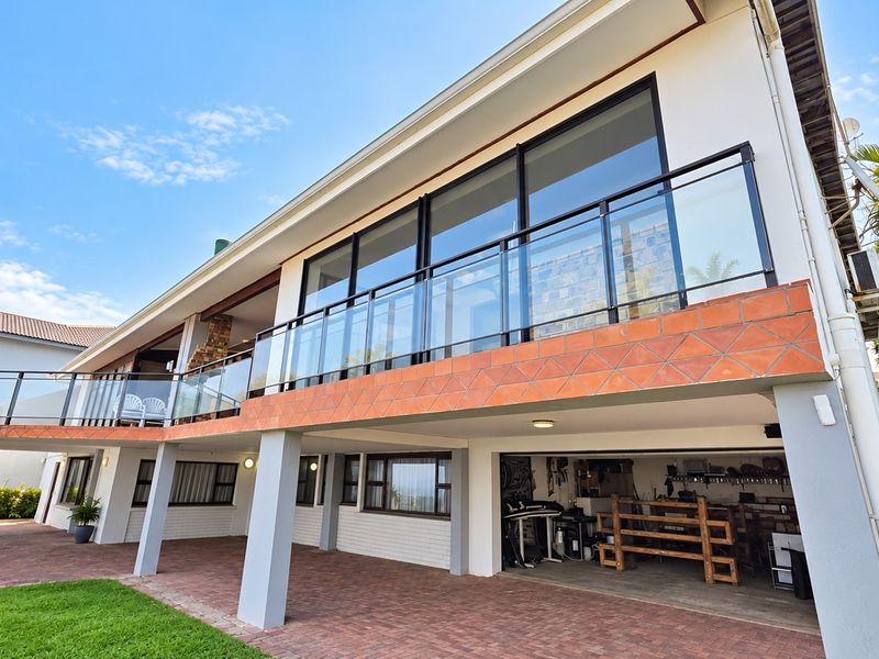 Rear elevation featuring a spacious paved patio, a glass-balustraded balcony, and a ground-level garage area with integrated structural columns.