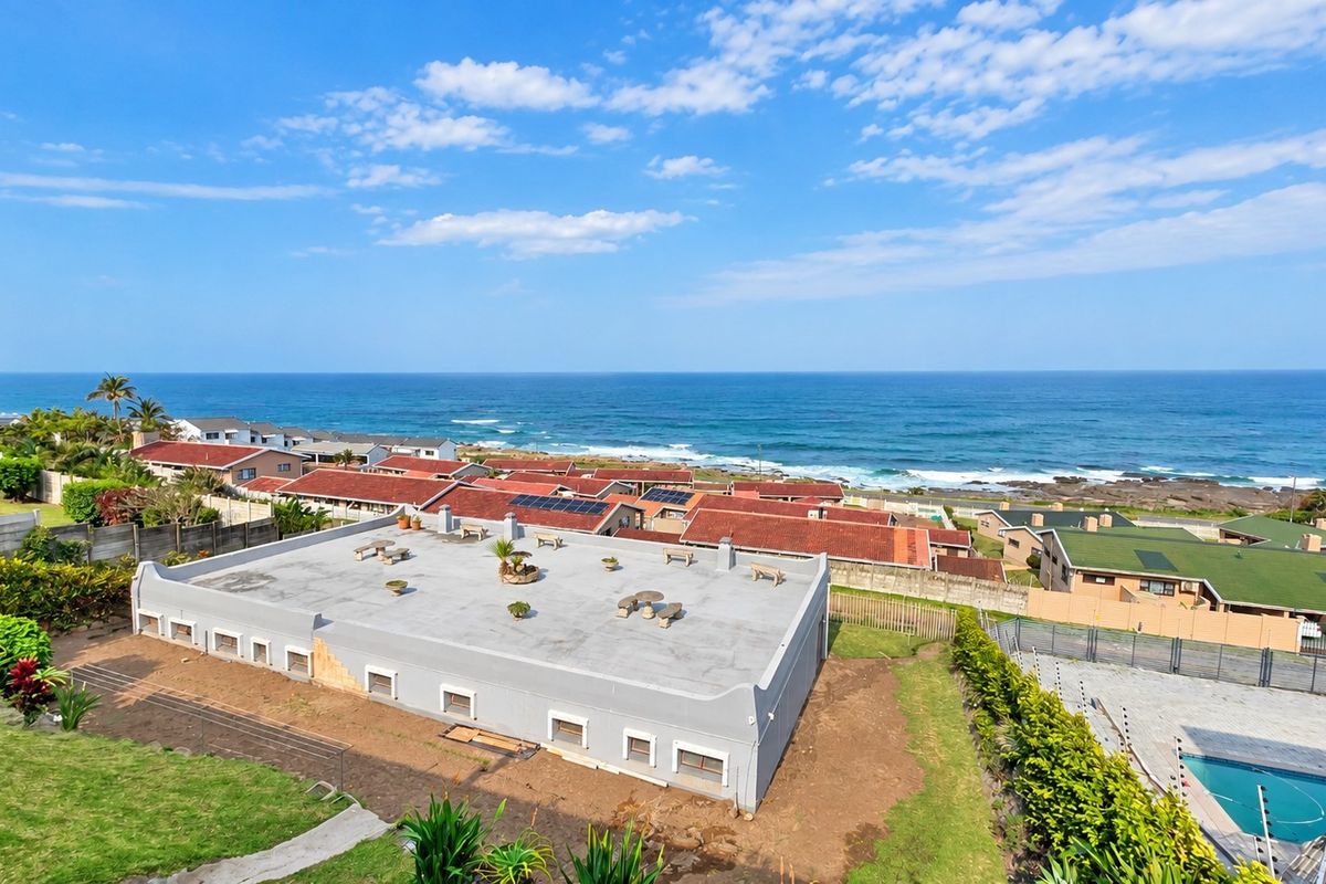 Aerial view of a coastal property featuring a flat roof with solar panels, surrounding residential area, and a swimming pool.