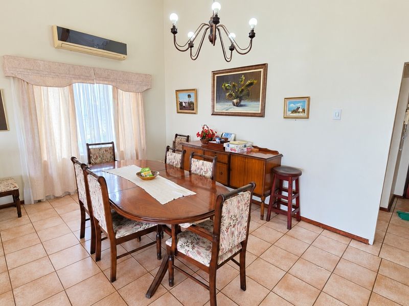 A dining room featuring ceramic tile flooring, a wall-mounted air conditioning unit, and a classic wrought iron chandelier.