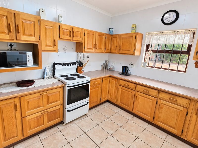 A functional kitchen featuring traditional wooden cabinetry, laminate countertops, a freestanding electric stove, and tiled flooring with a tiled backsplash.