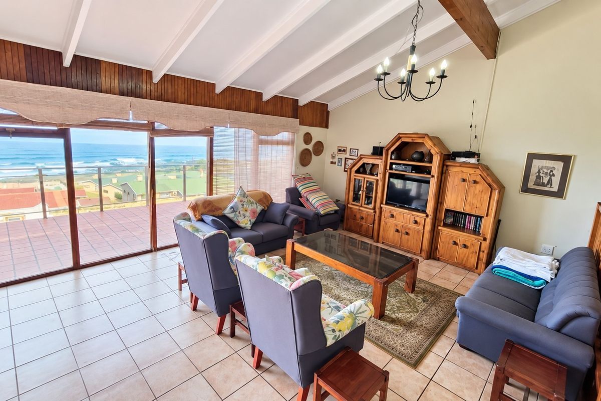 Spacious living room featuring vaulted ceilings with exposed timber beams, tiled flooring, and large sliding doors opening to a balcony with ocean views.