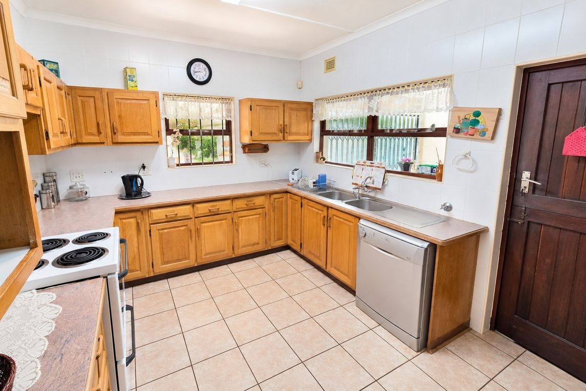 A functional kitchen featuring wooden cabinetry, laminate countertops, tiled flooring, and a double basin sink with security bars on the windows.
