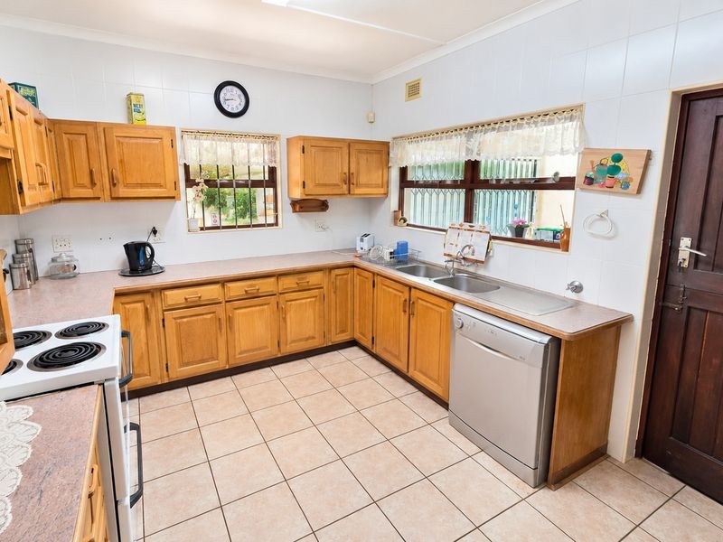 A functional kitchen featuring wooden cabinetry, laminate countertops, tiled flooring, and a double basin sink with security bars on the windows.