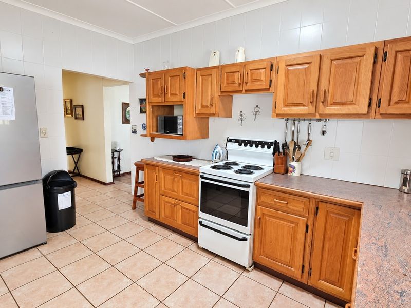 A functional kitchen featuring wooden cabinetry, laminate countertops, tiled backsplash, and tiled flooring, with a freestanding stove and ample storage space.