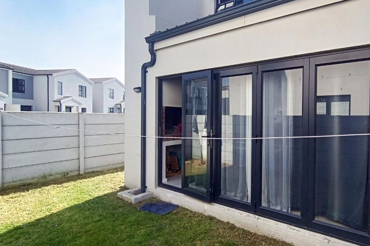 Rear exterior view featuring a built-in braai area, modern black aluminium stacker doors, and a private garden with precast boundary walling.