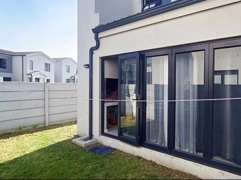 Rear exterior view featuring a built-in braai area, modern black aluminium stacker doors, and a private garden with precast boundary walling.