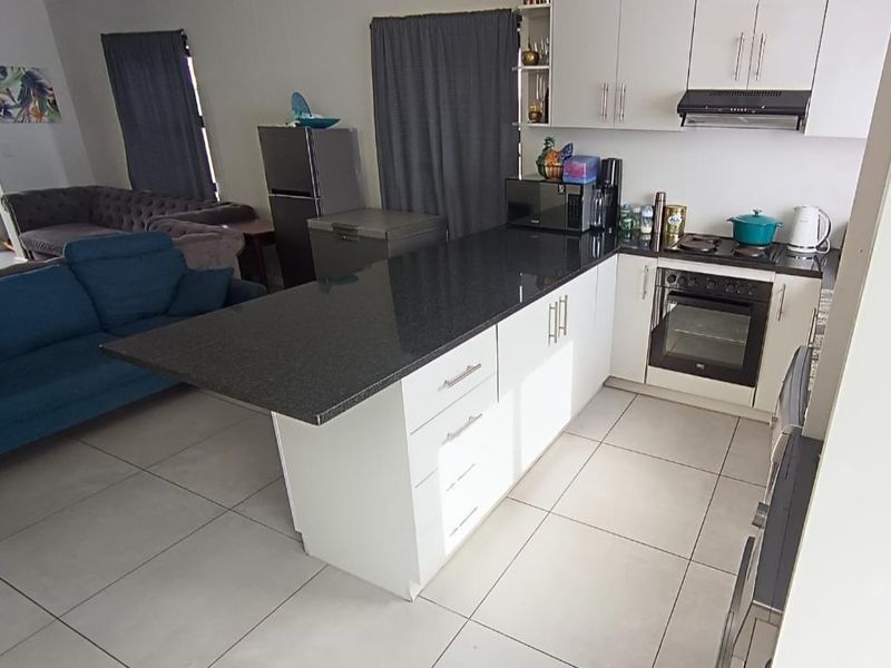 Open-plan kitchen featuring granite countertops, built-in oven, hob, extractor fan, and tiled flooring, seamlessly flowing into the adjacent living area.