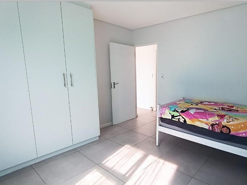 A clean bedroom featuring neutral tiled flooring and a large built-in wardrobe, offering a bright and functional living space.