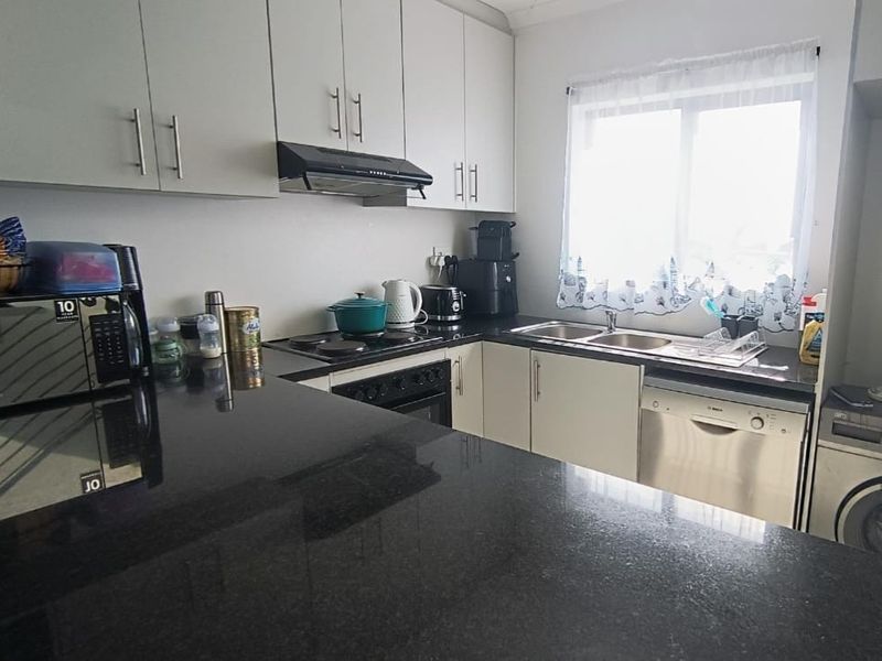 A functional kitchen featuring dark granite countertops, ample built-in cabinetry, an electric hob with extractor fan, and a double sink.