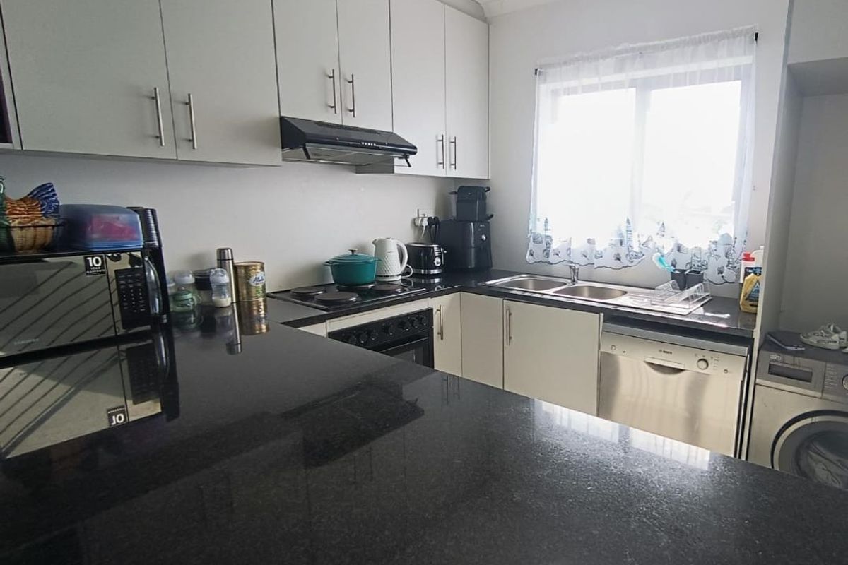 A functional kitchen featuring dark granite countertops, ample built-in cabinetry, an electric hob with extractor fan, and a double sink.