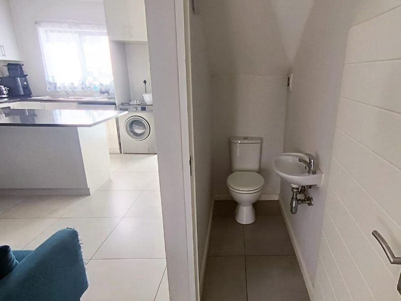 A compact guest bathroom featuring a toilet and a wall-mounted basin, conveniently located adjacent to the kitchen area.