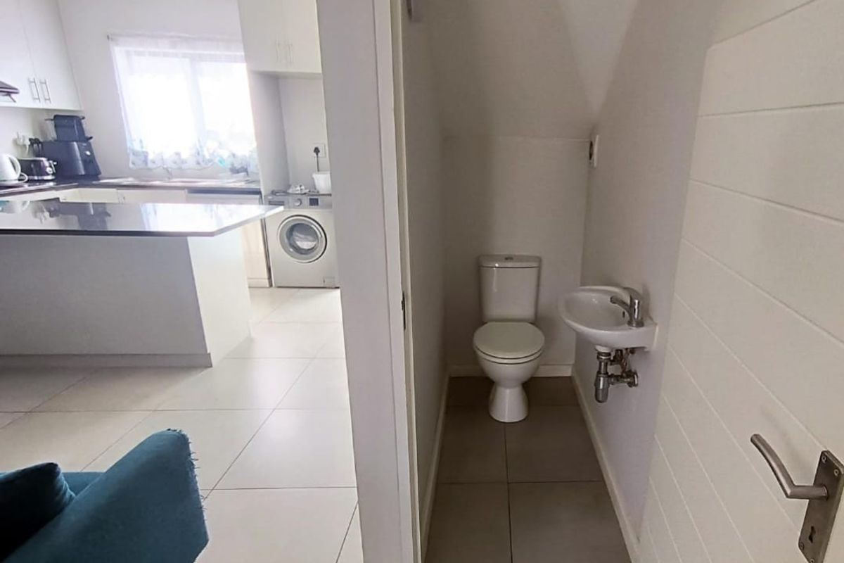 A compact guest bathroom featuring a toilet and a wall-mounted basin, conveniently located adjacent to the kitchen area.