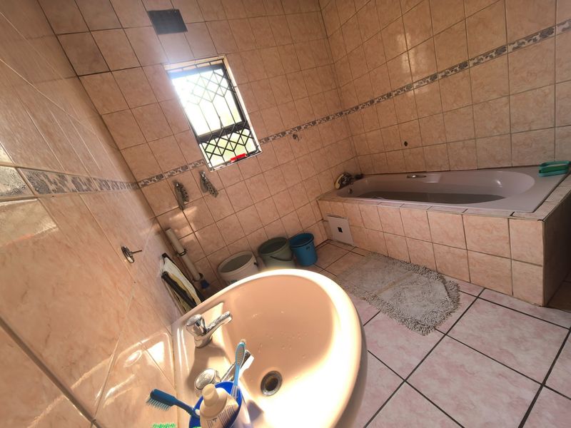 A dated bathroom featuring a built-in bathtub, pedestal basin, and full-height ceramic wall tiling with security bars on the window.