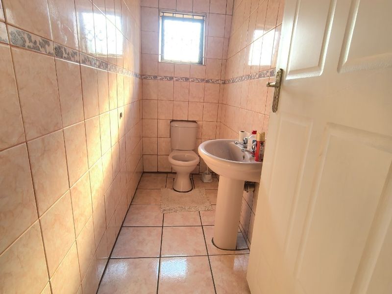 A compact bathroom featuring a pedestal basin, toilet, and full-height ceramic wall tiling.