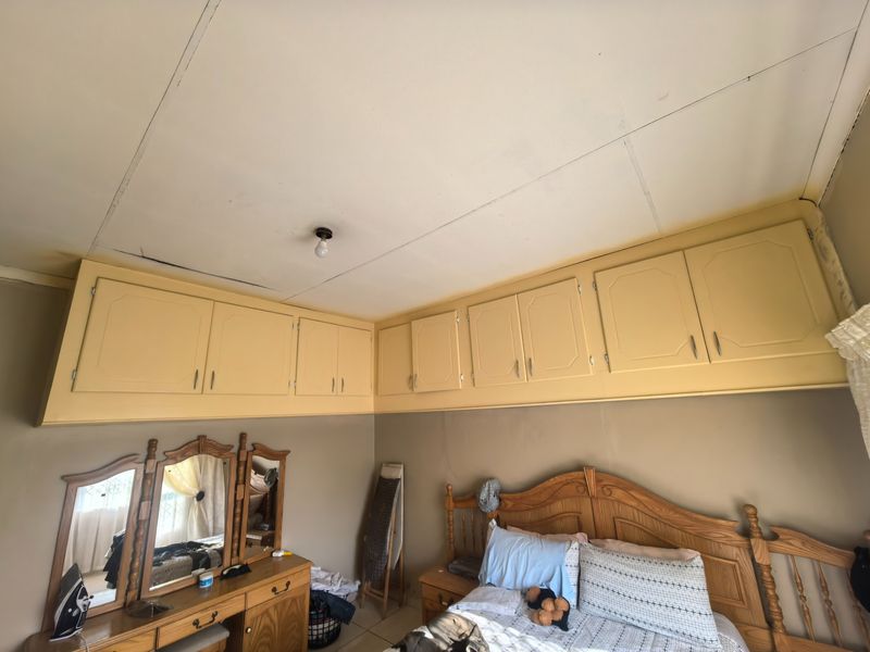Bedroom featuring built-in overhead storage cabinetry and a central ceiling light fixture, showing signs of wear on the ceiling panels.