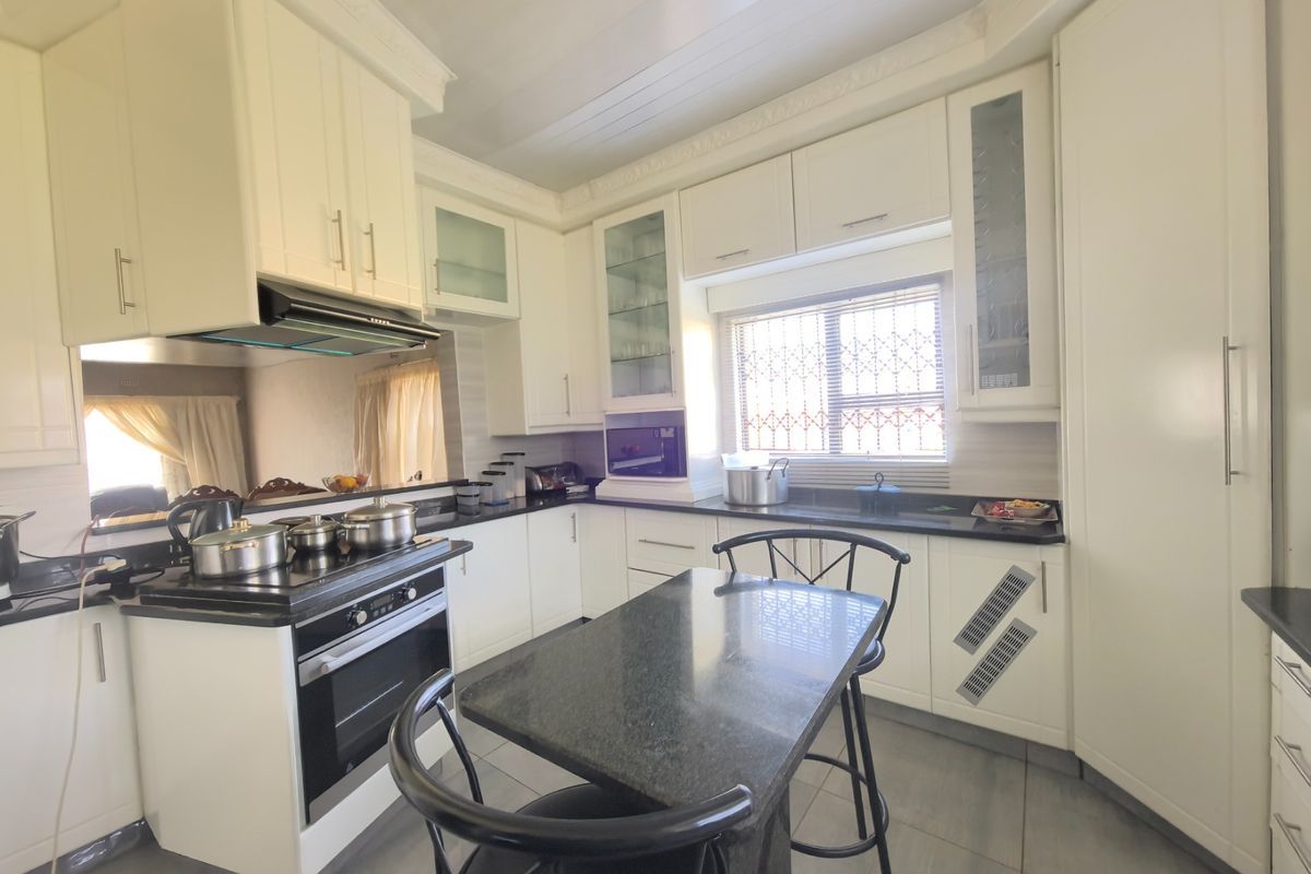 A well-maintained kitchen featuring white cabinetry, dark granite countertops, built-in oven, extractor fan, and tiled flooring with a central breakfast nook.