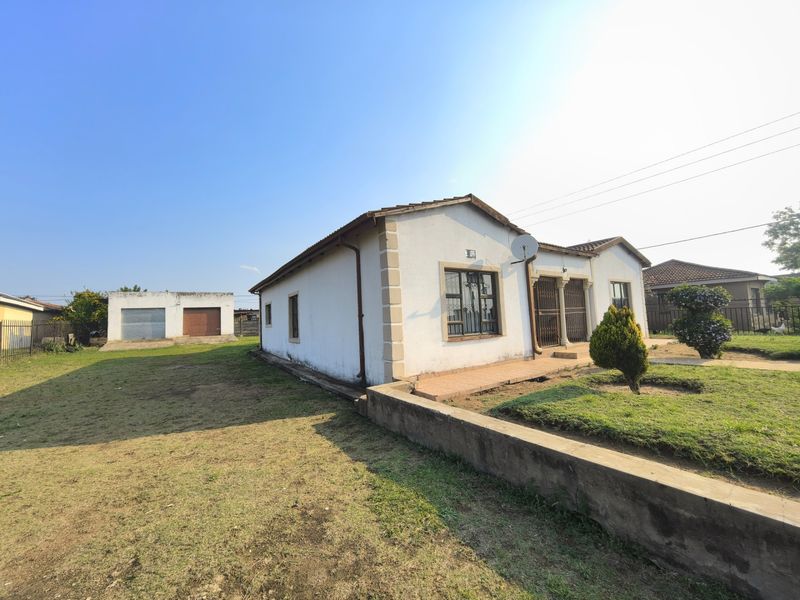Front view of a single-story house featuring a tiled roof, security gates, and a detached garage on a spacious plot.