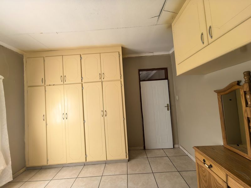 A bedroom featuring extensive built-in cabinetry, tiled flooring, and an internal door, requiring ceiling repairs and cosmetic updates to modernize the space.