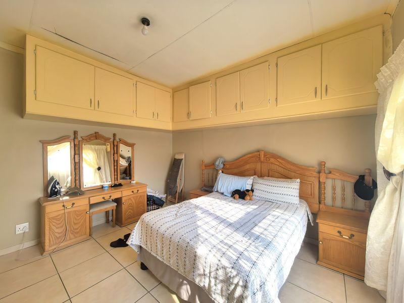 A bedroom featuring built-in overhead cupboards and tiled flooring, offering functional storage space with potential for cosmetic updates.