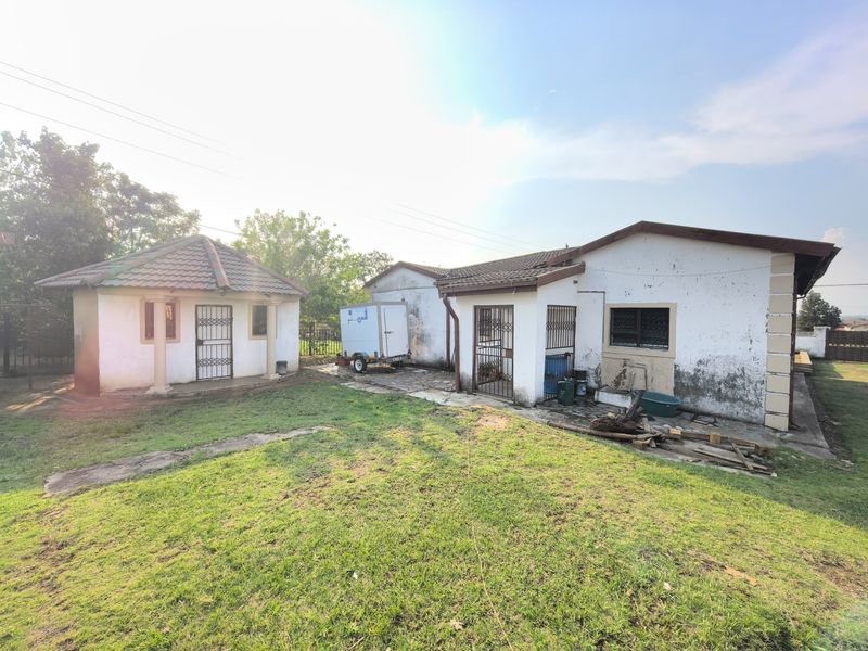 Rear view of the property showing a detached outbuilding, main house structure, lawn area, and paved pathways.