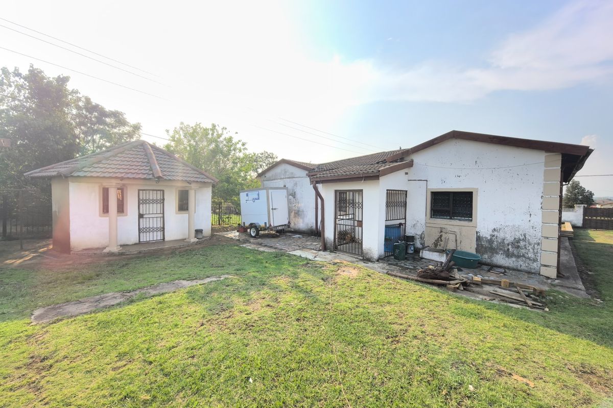 Rear view of the property showing a detached outbuilding, main house structure, lawn area, and paved pathways.