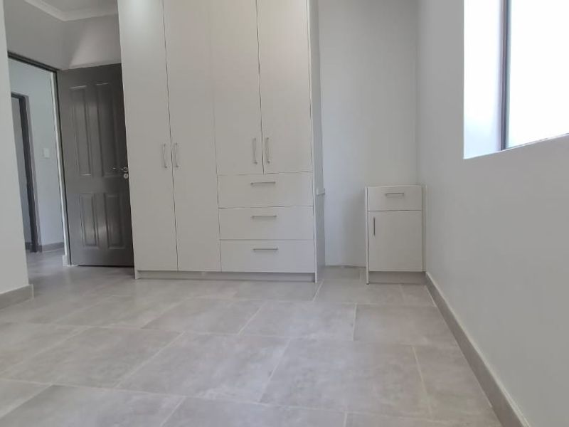 A clean, empty bedroom featuring neutral tiled flooring and white built-in cupboards, offering a bright and versatile space ready for personalization.
