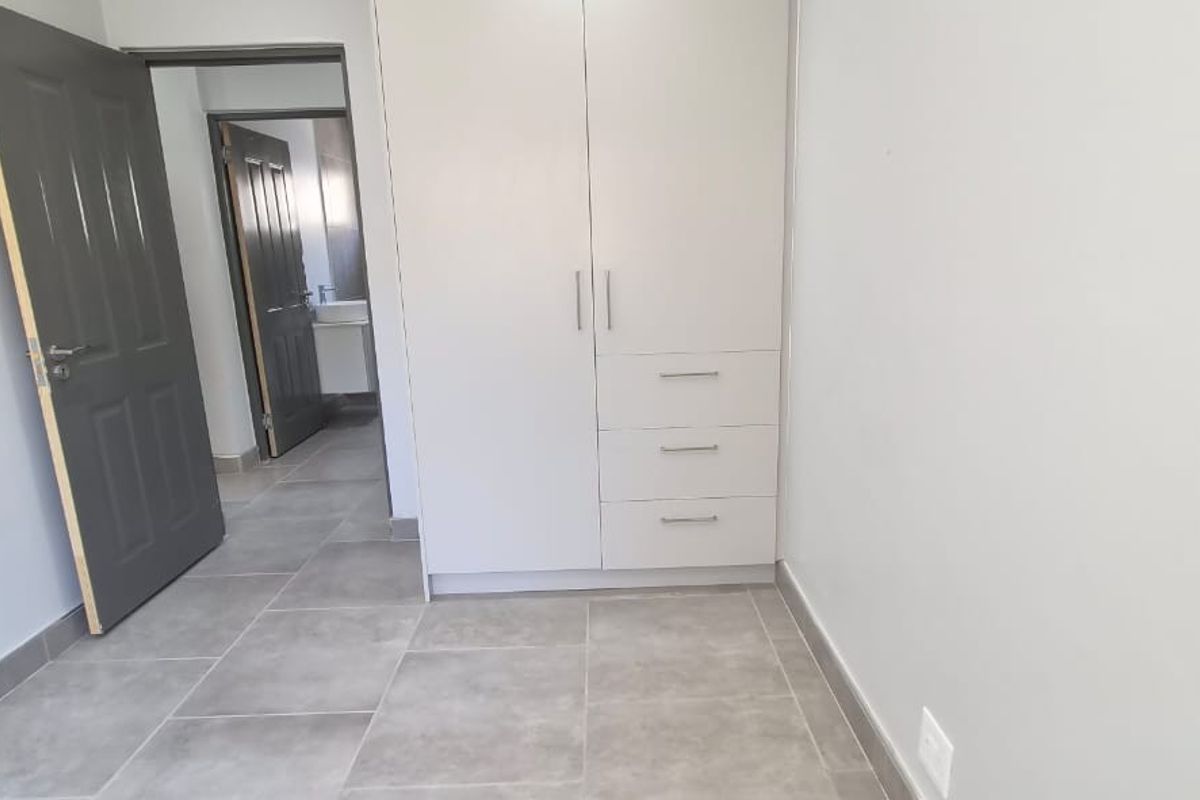 A clean, empty bedroom featuring modern grey floor tiles, a built-in white wardrobe, and access to an adjoining bathroom.