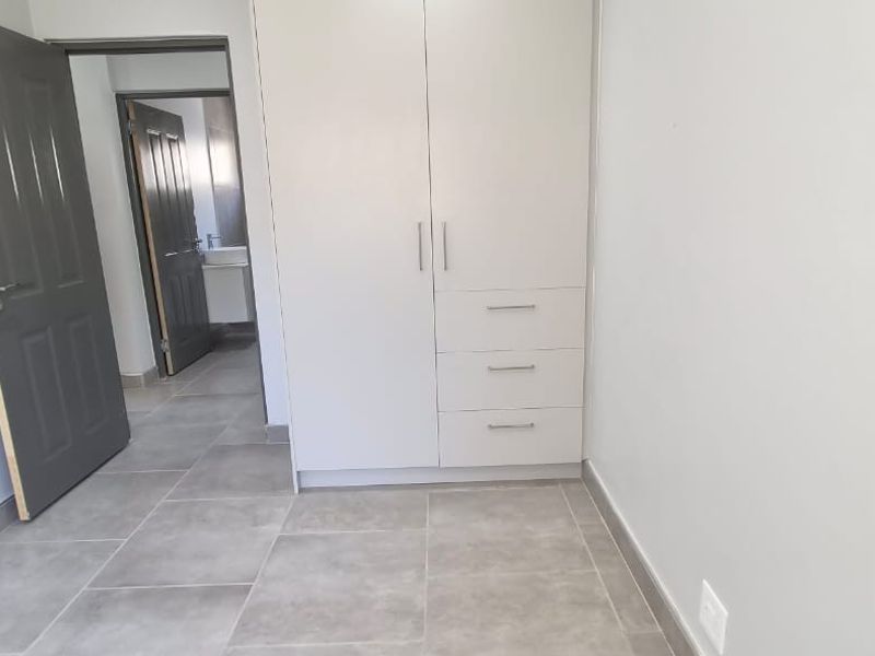 A clean, empty bedroom featuring modern grey floor tiles, a built-in white wardrobe, and access to an adjoining bathroom.