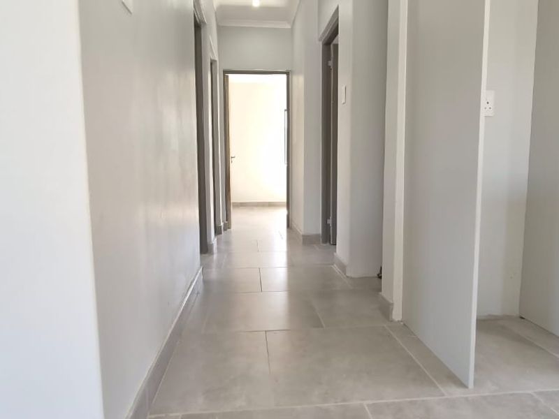 A clean, neutral-toned hallway featuring modern tiled flooring and access to multiple rooms, providing a bright and functional transition space.