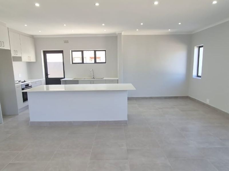 Spacious open-plan living area featuring a modern kitchen with a central island, built-in cabinetry, and neutral tiled flooring throughout.