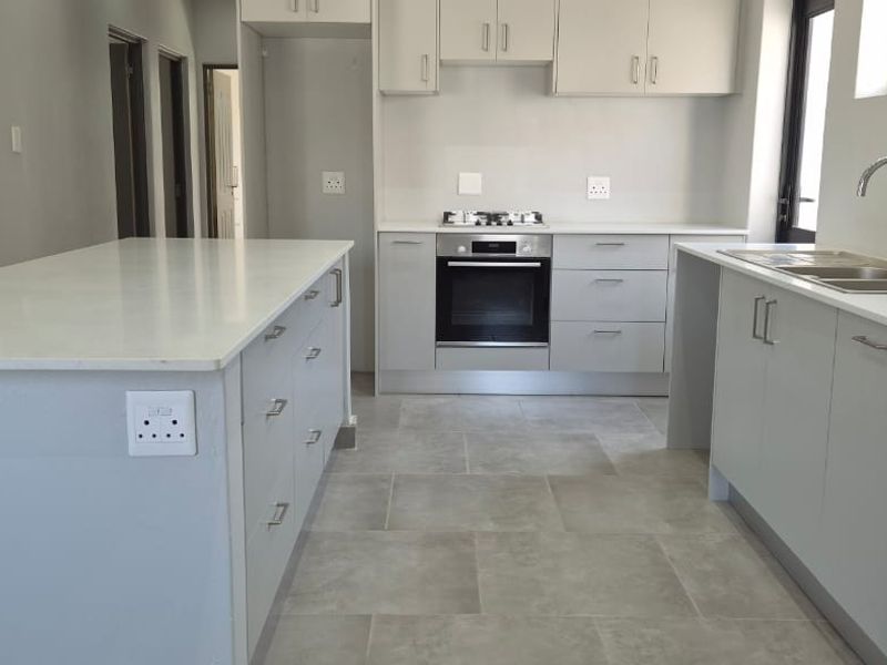 Modern kitchen featuring a central island, built-in oven, gas hob, double sink, and ample fitted cabinetry with neutral grey finishes.
